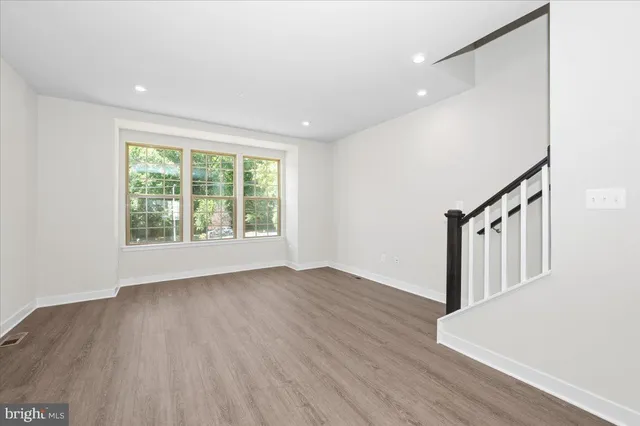 a view of empty room with wooden floor and kitchen