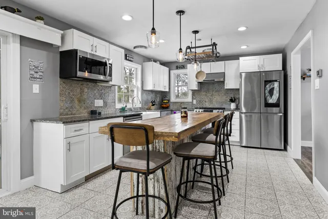 a kitchen with stainless steel appliances kitchen island granite countertop a dining table chairs refrigerator and microwave