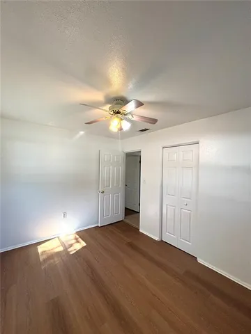 an empty room with wooden floor chandelier fan and windows