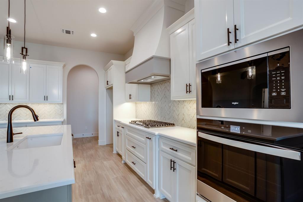 128 Prairie Winds Drive Poolville, TX 76487 - Photo 22 of 40 a kitchen with stainless steel appliances kitchen island granite countertop a stove and a sink with wooden floor
