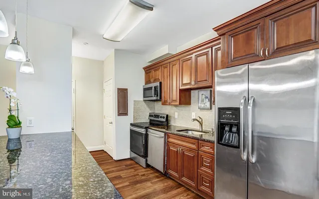 a kitchen with stainless steel appliances granite countertop a refrigerator a sink dishwasher a stove and a dining table with wooden floor