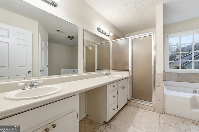 a bathroom with a double vanity sink a mirror a bathtub and next to a window