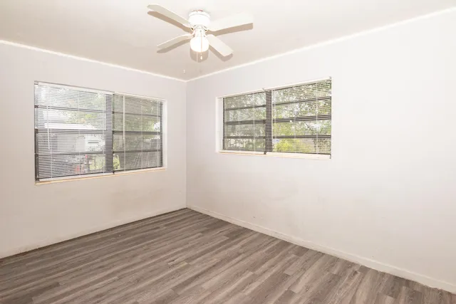 an empty room with wooden floor chandelier fan and windows