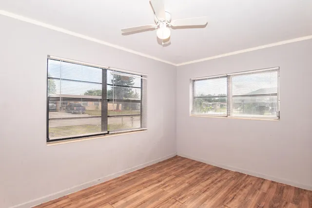 an empty room with wooden floor chandelier fan and windows