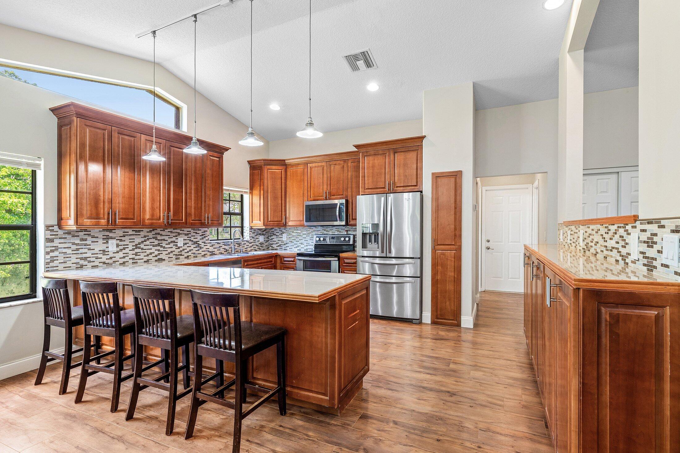 18142 43rd Road North Loxahatchee, FL 33470 - Photo 4 of 42 a kitchen with stainless steel appliances kitchen island granite countertop wooden floor a refrigerator and a sink