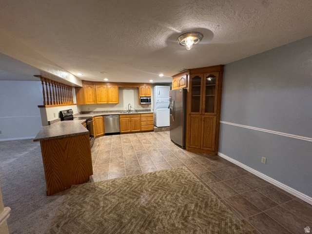 655 North 8th East Preston, ID 83263 - Photo 16 of 32 Kitchen with stainless steel appliances, a textured ceiling, wood finish cabinetry, stacked washing machine and dryer, and a peninsula