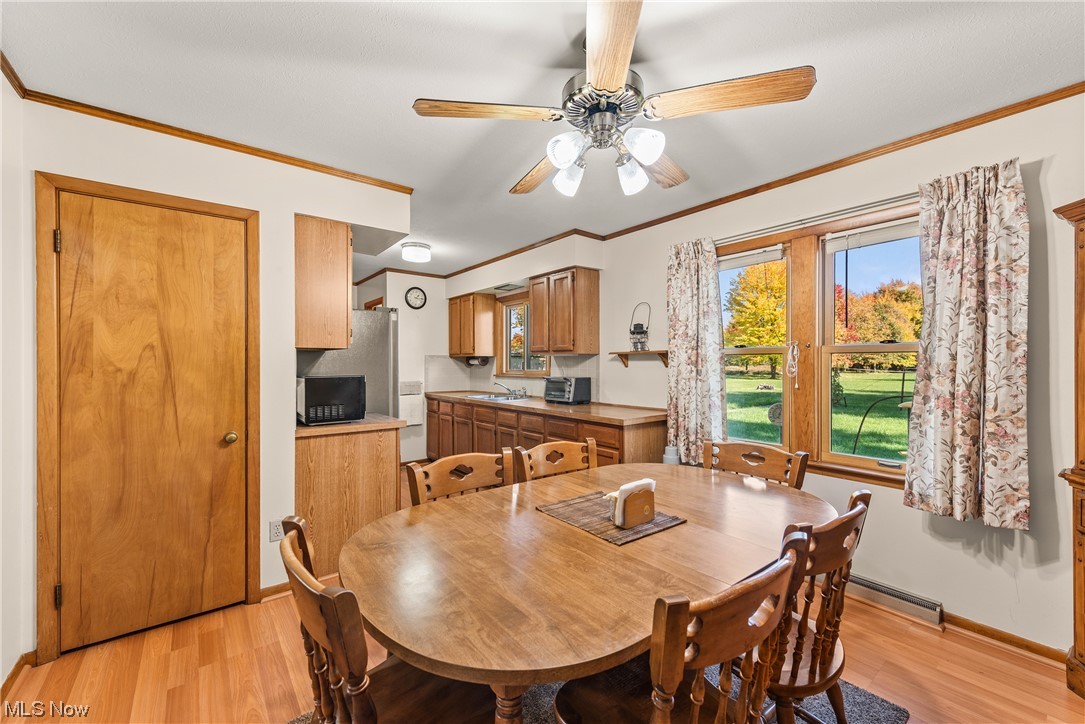 2151 Lester Road Valley City, OH 44280 - Photo 9 of 24 Dining area featuring sink, ceiling fan, a baseboard radiator, light wood-type flooring, and crown molding