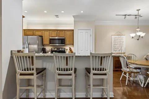 a kitchen with stainless steel appliances granite countertop a stove top oven a sink a dining table and chairs with wooden floor