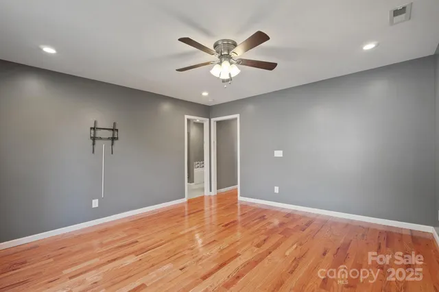 a view of an empty room with wooden floor and a ceiling fan