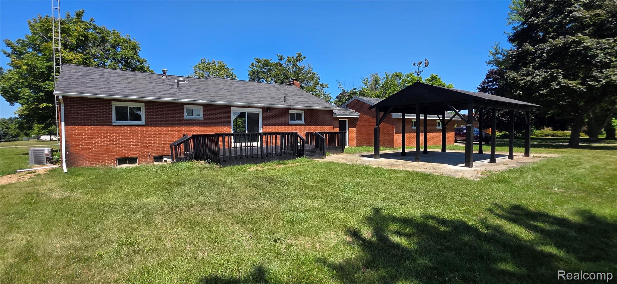 4363 West Dodge Road Clio, MI 48420 - Photo 16 of 52 Expansive green lawn featuring a large black wood-finish deck with steps, a sliding glass door entry, and a detached open-air pavilion structure