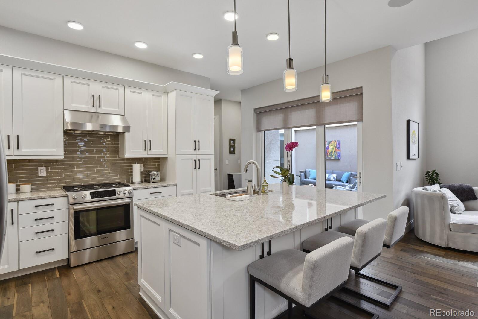 76 Niagara Street Denver, CO 80230 - Photo 6 of 44 a large kitchen with kitchen island a stove a sink a refrigerator and white cabinets with wooden floor