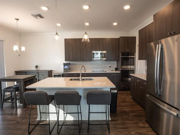 a kitchen with kitchen island a stove a refrigerator a sink a dining table and chairs with wooden floor