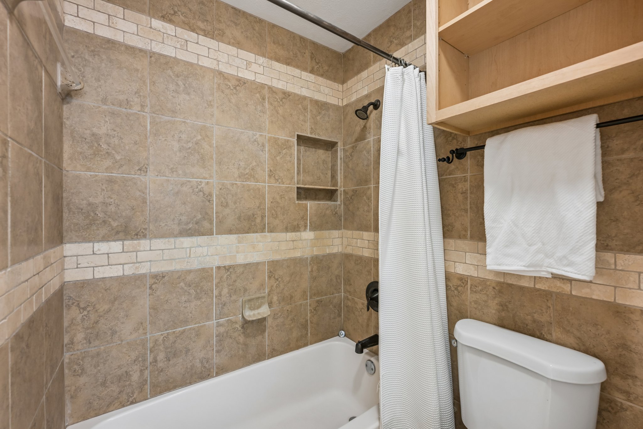 13101 Travis View Loop Austin, TX 78732 - Photo 16 of 27 Textured tile surrounds the clean white tub and toilet, offering a harmonious and functional bath space.