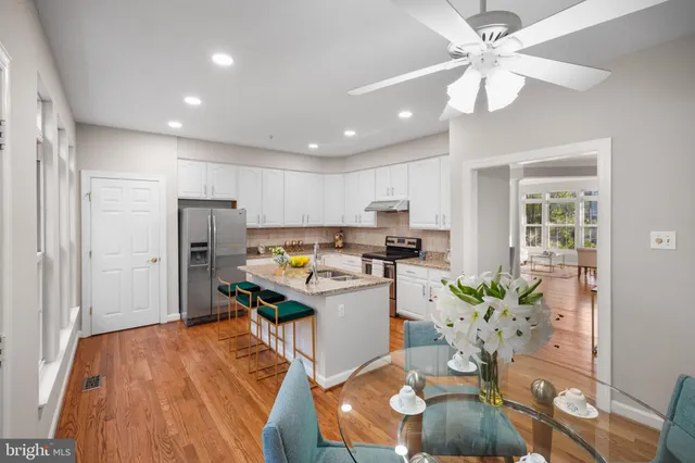 a kitchen with stainless steel appliances granite countertop a refrigerator a sink a stove a dining table and chairs with wooden floor