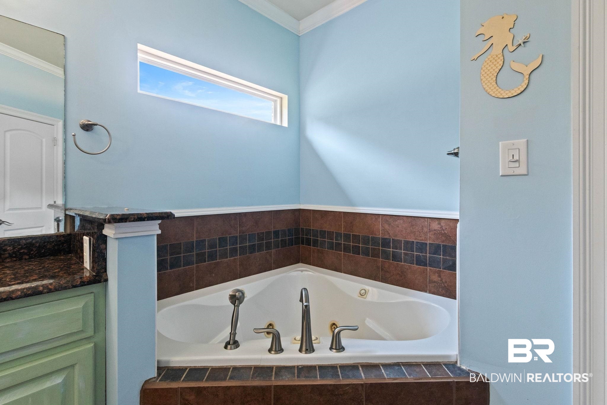 79 Whitetail Run Chatom, AL 36518 - Photo 44 of 82 Corner soaking tub featuring tile surround with dark brown and black accent tiles, a polished chrome faucet, and a horizontal transom window