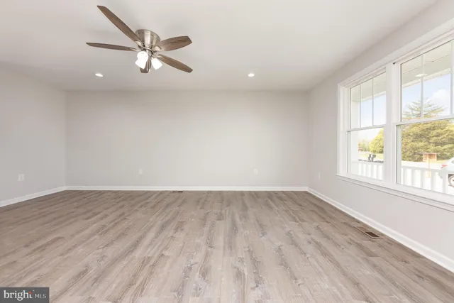 an empty room with wooden floor fan and windows