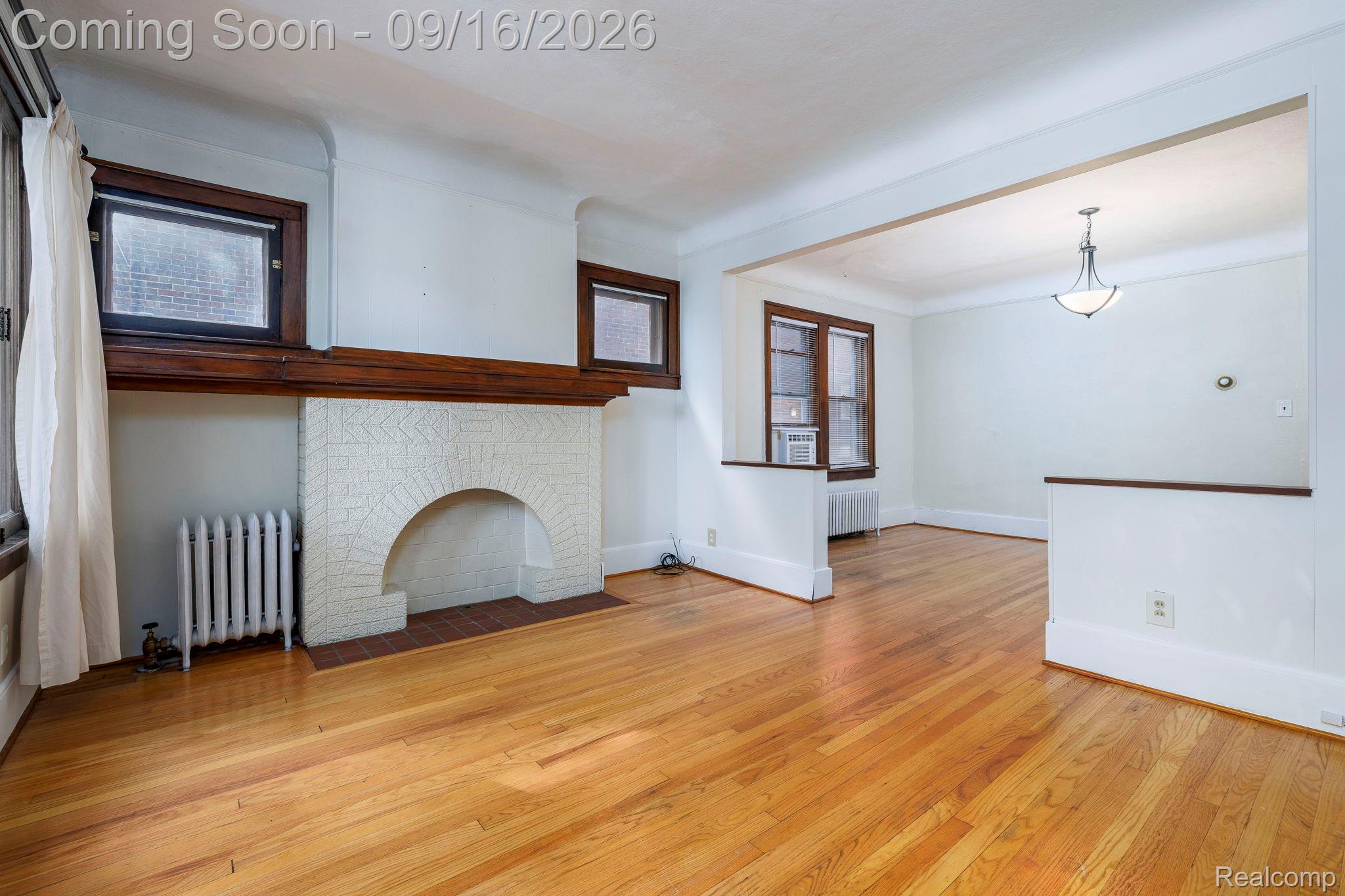 Wood-finish flooring throughout, a decorative fireplace with a textured surround, prominent wood trim, and an overhead light fixture