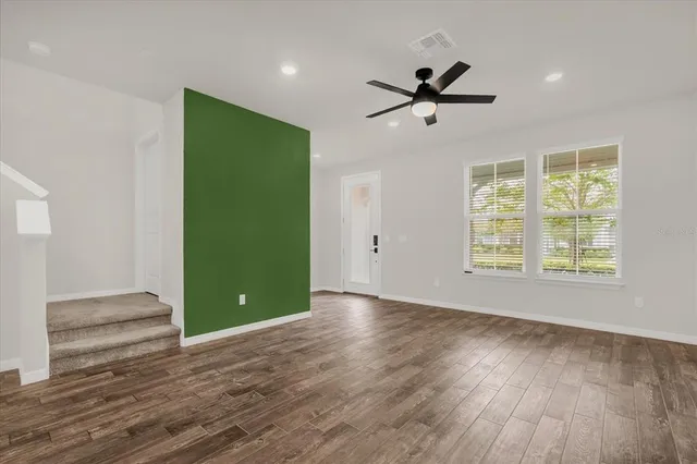 an empty room with wooden floor a ceiling fan and windows