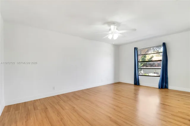 an empty room with wooden floor chandelier fan and windows