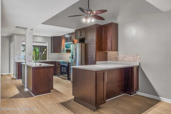 a kitchen with stainless steel appliances a stove a refrigerator a sink a microwave oven and a dining table with wooden floor