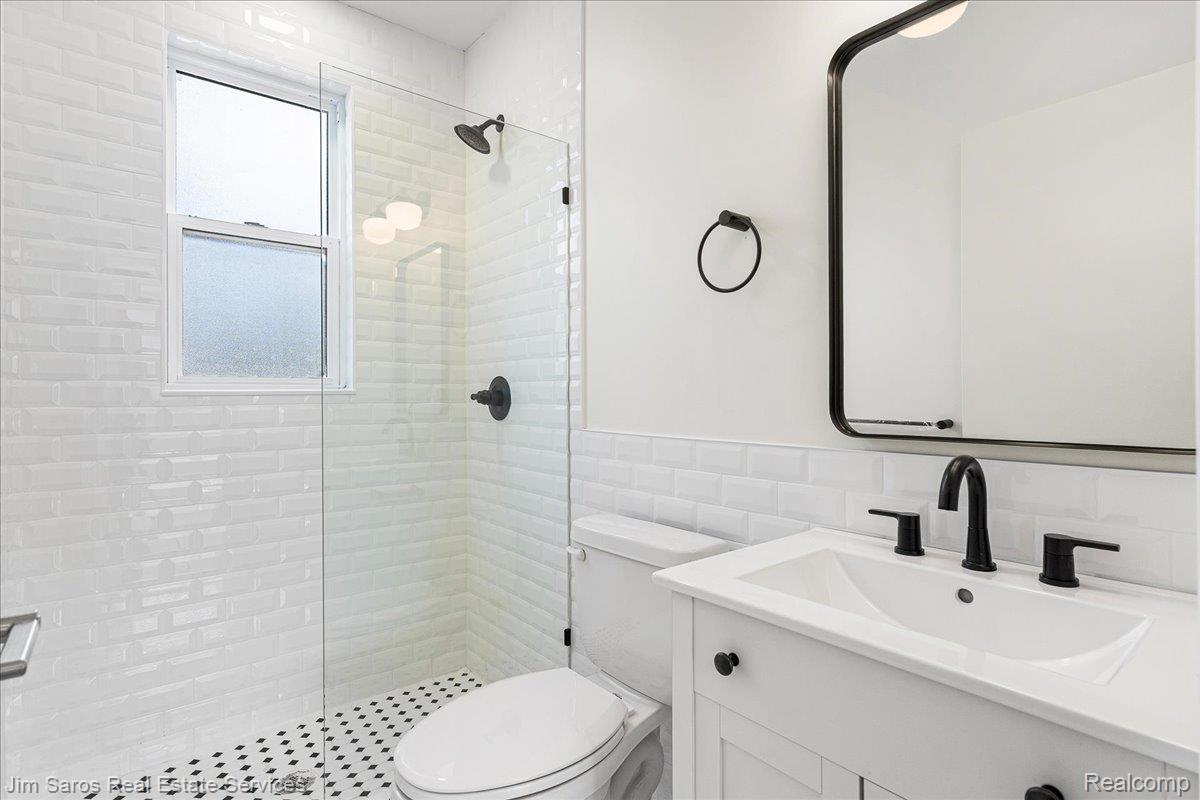 4735 Rohns Street, Unit 1B Detroit, MI 48214 - Photo 9 of 14 Bathroom featuring a glass-enclosed shower, white subway tile walls, a vanity with integrated sink, and matte black fixtures