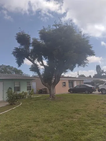 a view of a white house next to a yard with big trees