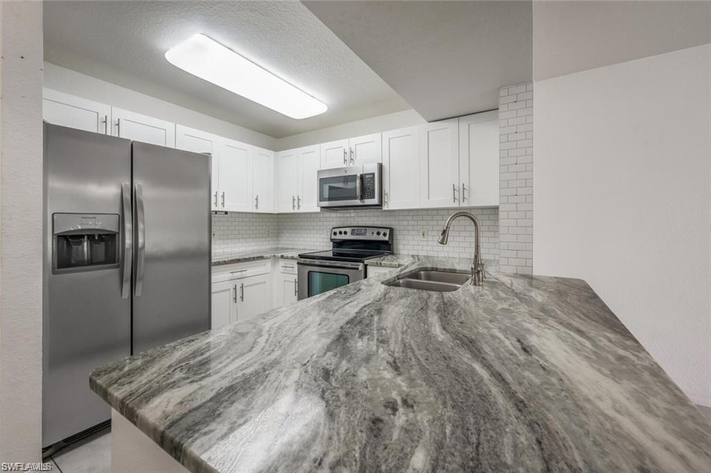 8244 Key Royal Circle, Unit 615 Naples, FL 34119 - Photo 3 of 23 Kitchen with appliances with stainless steel finishes, light stone counters, backsplash, white cabinetry, and a textured ceiling