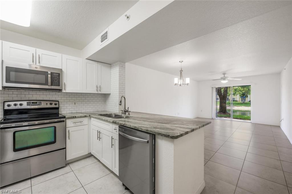 8244 Key Royal Circle, Unit 615 Naples, FL 34119 - Photo 4 of 23 Kitchen featuring stainless steel appliances, a textured ceiling, backsplash, light tile patterned floors, and a peninsula