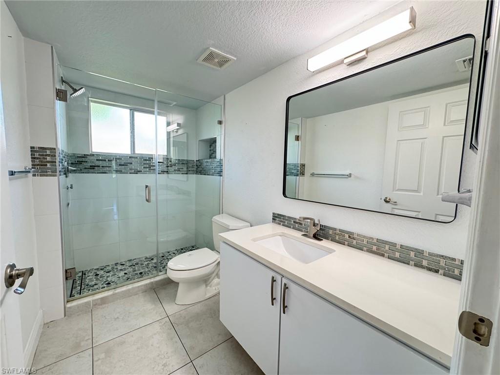 8244 Key Royal Circle, Unit 615 Naples, FL 34119 - Photo 6 of 23 Full bathroom featuring vanity, a textured ceiling, a stall shower, light tile patterned floors, and backsplash