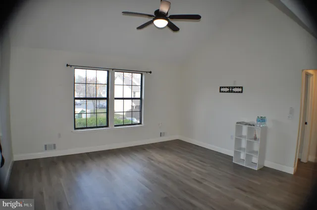 an empty room with wooden floor a ceiling fan and windows