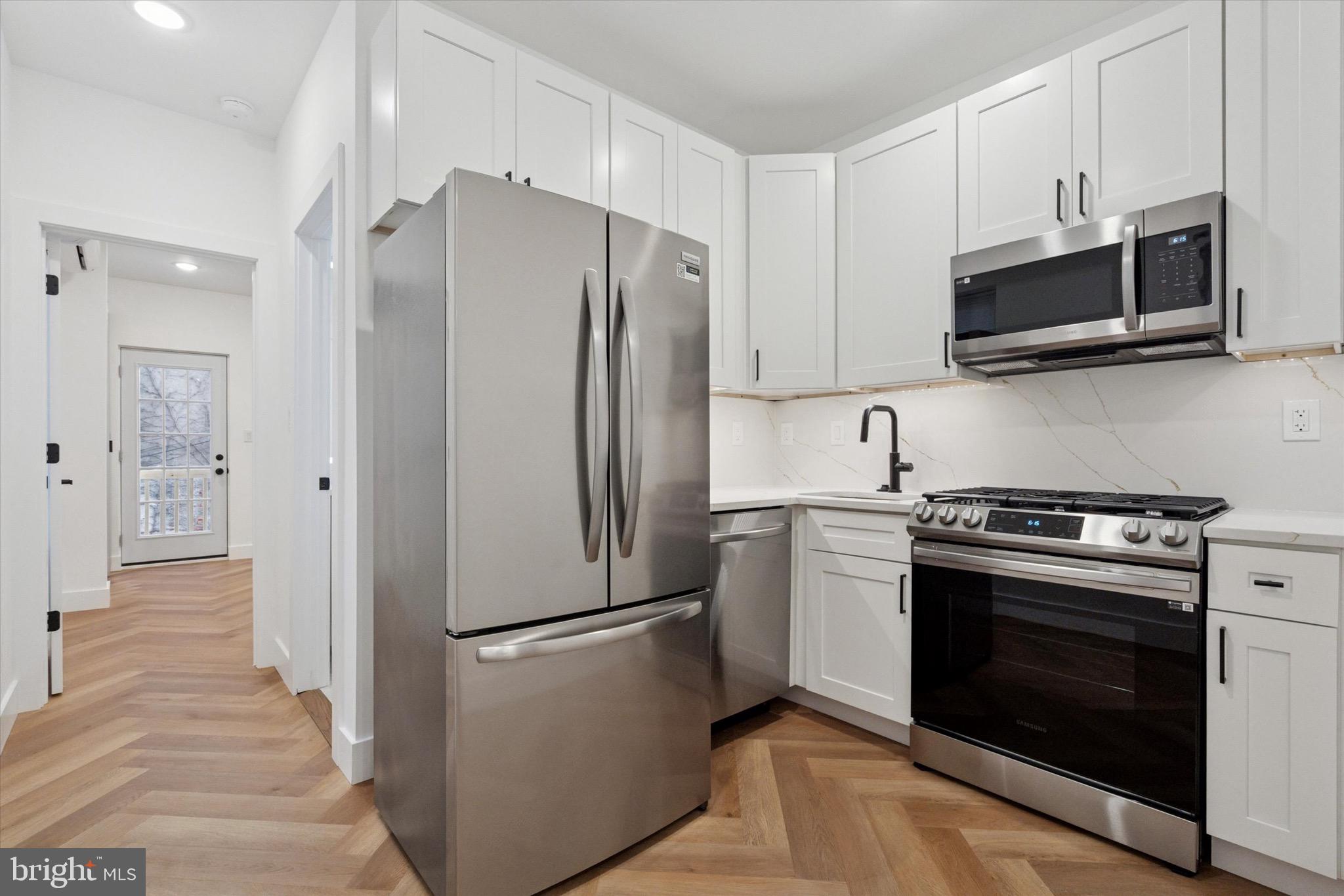 1438 Tasker Street, Unit 2 Philadelphia, PA 19145 - Photo 2 of 11 a kitchen with stainless steel appliances white cabinets white stove a microwave and a refrigerator
