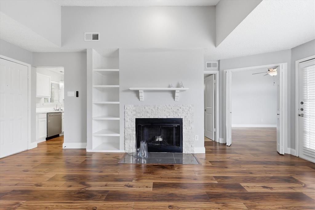 5550 Spring Valley Road, Unit A31 Dallas, TX 75254 - Photo 4 of 24 Living area featuring a fireplace with a textured stone surround, wood-finish flooring, and built-in shelving