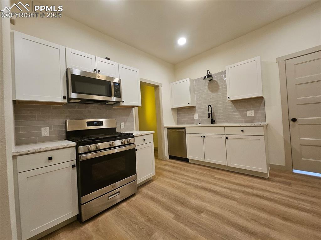 1138 Pine Street Pueblo, CO 81004 - Photo 9 of 22 a kitchen with stainless steel appliances white cabinets a sink a stove a microwave and wooden floors