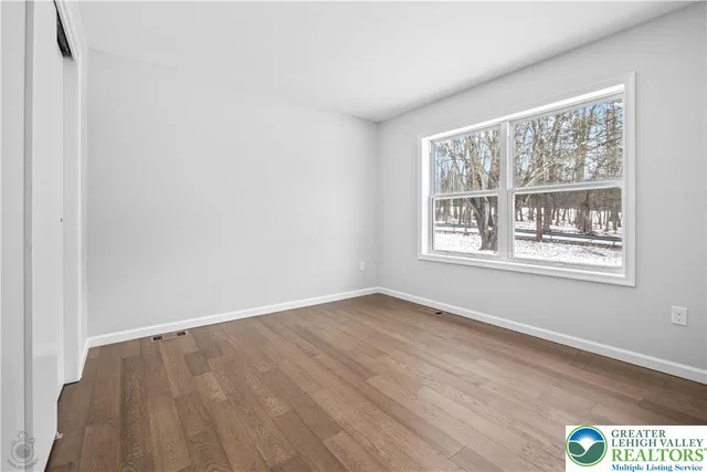 a view of an empty room with wooden floor and window