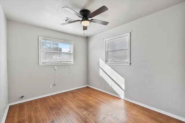 an empty room with wooden floor chandelier fan and windows
