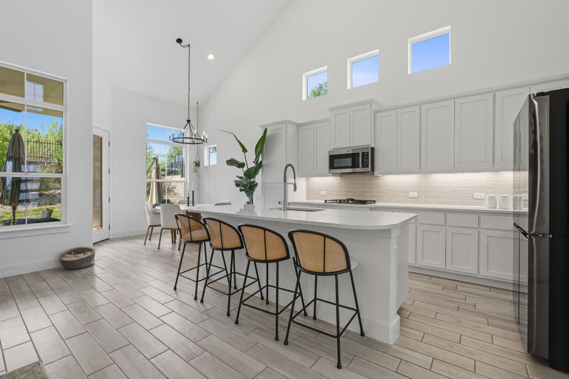 101 Cartwheel Bend, Unit 52 Austin, TX 78738 - Photo 8 of 31 a kitchen with stainless steel appliances granite countertop a stove a sink a microwave a dining table and chairs with wooden floor