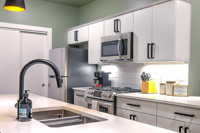 a kitchen with stainless steel appliances granite countertop a kitchen island a stove a sink dishwasher and white cabinets with wooden floor