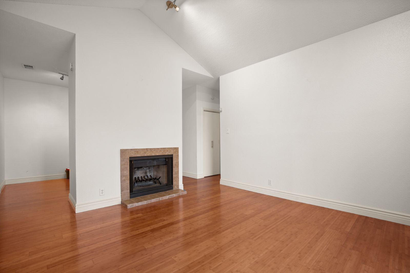 11970 Jollyville Road, Unit 216 Austin, TX 78759 - Photo 4 of 20 Unfurnished living room featuring a fireplace, vaulted ceiling, wood finished floors, and rail lighting