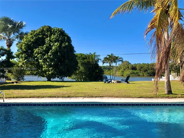 a view of a swimming pool with a yard and palm trees