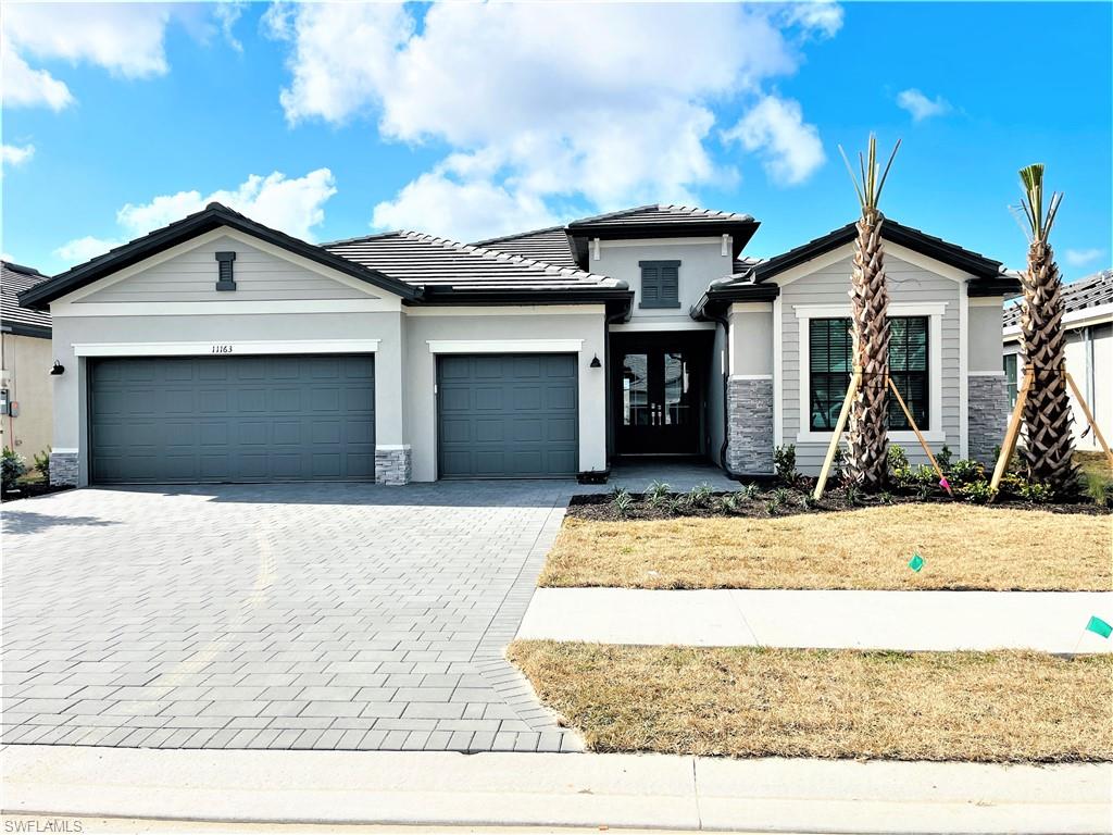 View of front of house with stone siding, driveway, a garage, and stucco siding