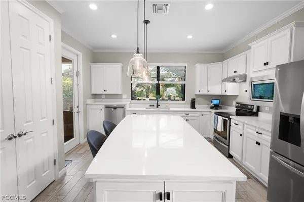 a kitchen with stainless steel appliances kitchen island granite countertop a stove a sink a refrigerator and white cabinets with wooden floor