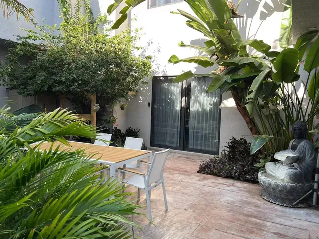 a view of a backyard with table and chairs potted plants and large tree
