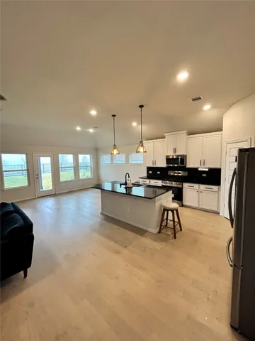 a kitchen with stainless steel appliances kitchen island granite countertop a stove a refrigerator a sink a oven and a dining table with wooden floor