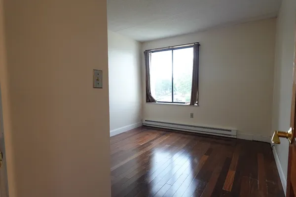 a view of an empty room with wooden floor and closet