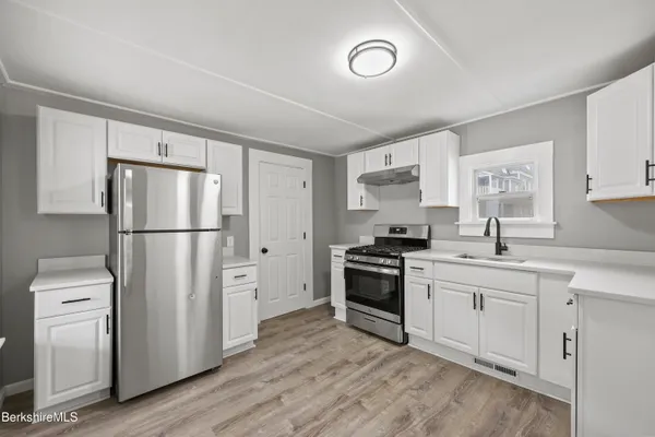 a kitchen with stainless steel appliances granite countertop a refrigerator a stove a sink and white cabinets with wooden floor