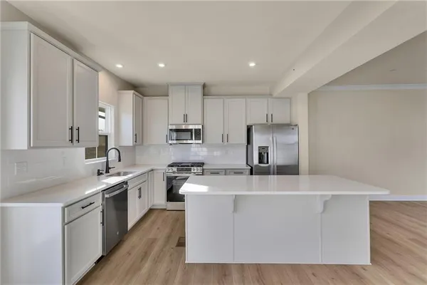 a large kitchen with stainless steel appliances granite countertop a stove a sink a refrigerator and white cabinets with wooden floor