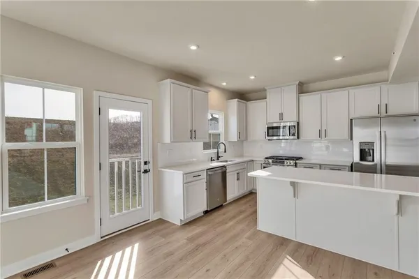 a large kitchen with stainless steel appliances granite countertop a stove a sink a refrigerator and white cabinets with wooden floor