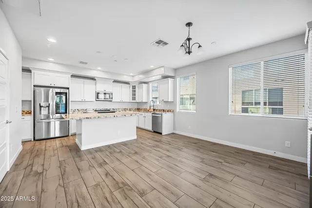 a large white kitchen with kitchen island a stove a sink dishwasher and white cabinets with wooden floor
