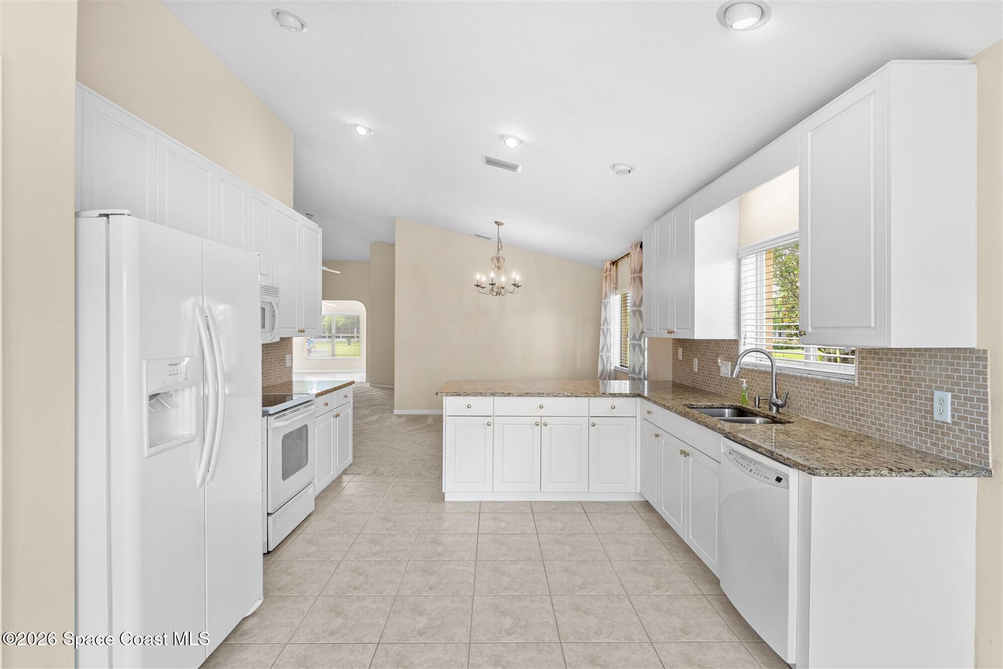 6904 Renshaw Drive Melbourne, FL 32940 - Photo 7 of 46 a large white kitchen with stainless steel appliances granite countertop a sink and dishwasher a refrigerator with white cabinets