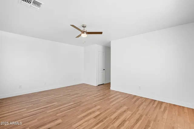 an empty room with wooden floor ceiling fan and windows